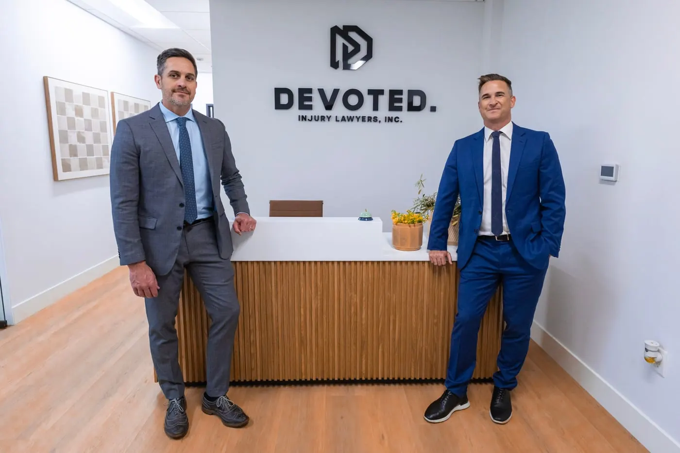 Two Devoted Injury Lawyers attorneys at the reception desk beneath the firm logo in the Oceanside, CA office